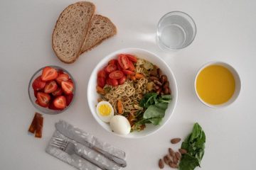 A balanced meal featuring a variety of healthy ingredients including noodles, eggs, almonds, strawberries, and fresh vegetables.