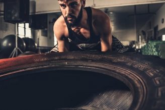 Man focusing intensely while flipping a large tire during a crossfit workout in a gym.