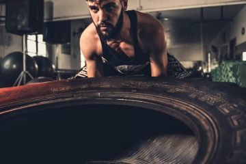 Man focusing intensely while flipping a large tire during a crossfit workout in a gym.