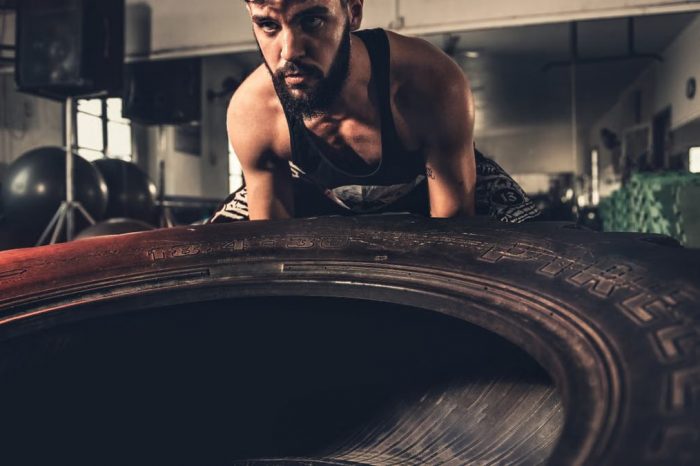 Man focusing intensely while flipping a large tire during a crossfit workout in a gym.